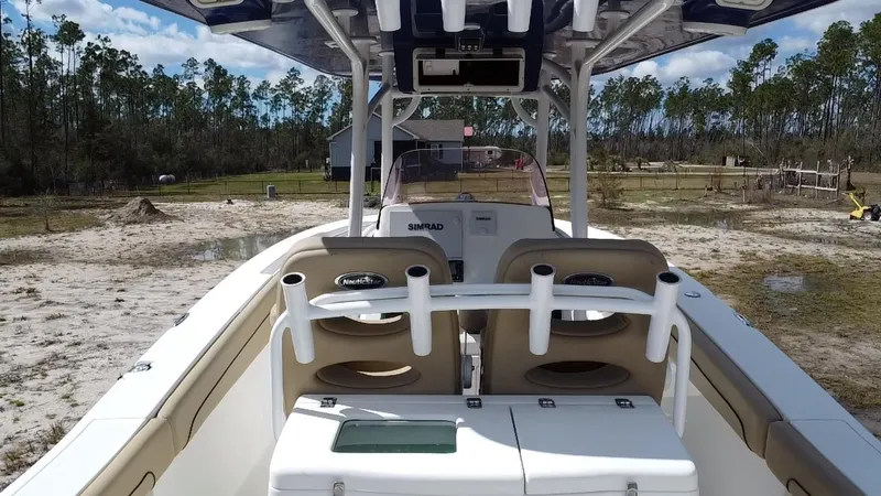 Slide: The Image of 2019 NauticStar 28 XS Offshore boat interior with rod holders and seating, surrounded by trees. - 34