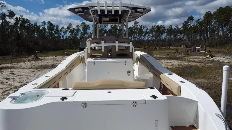Slide: The Image of 2019 NauticStar 28 XS Offshore boat with spacious deck and seating, set against a wooded backdrop. - 37