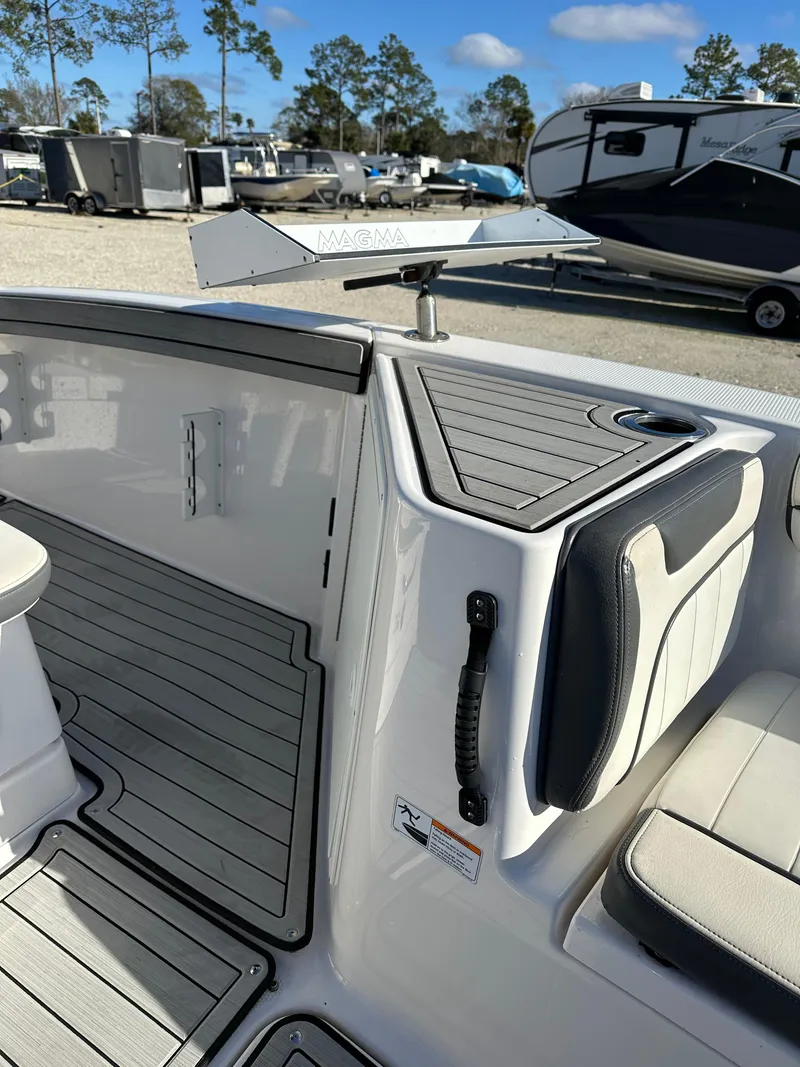 Slide: The Image of 2021 Yamaha Boats 210 FSH Sport interior with seating and storage, parked outdoors. - 16