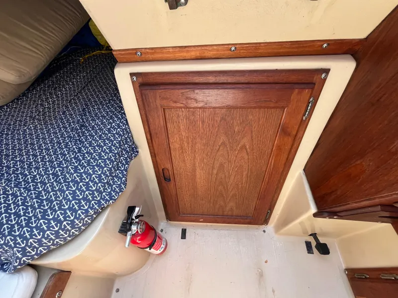 Slide: The Image of 1982 Catalina 27 interior with wooden cabinet, fire extinguisher, and anchor-patterned cushion. - 26