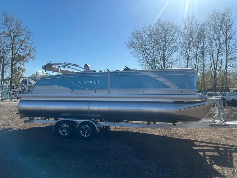 Slide: The Image of 2025 Godfrey Monaco 235 DFL Tritoon on trailer, parked outdoors under clear sky. - 8