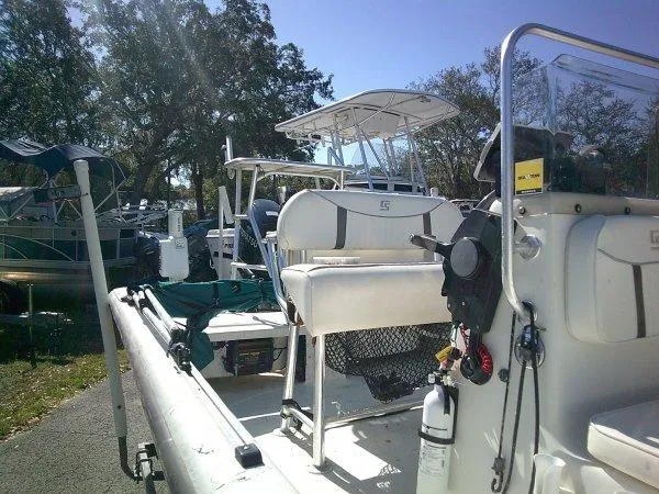 Slide: The Image of 2018 Carolina Skiff 198 DLX boat docked, featuring seating and console, surrounded by trees. - 4