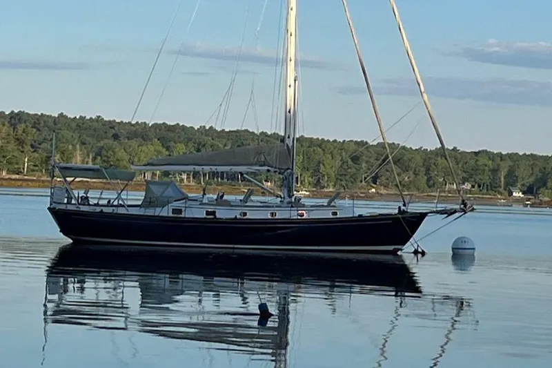 Slide: The Image of 1985 Shannon 43 Classic Cutter sailboat on calm water, forested shoreline in background. - 2