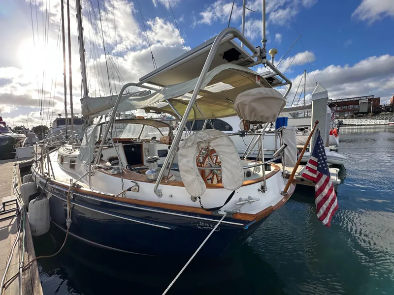 Slide: The Image of 1985 Shannon 43 Classic Cutter sailboat docked at marina, featuring American flag and clear skies. - 22