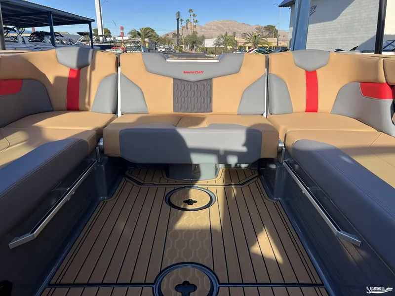Slide: The Image of 2025 MasterCraft XT25 boat interior with tan and gray seating, wood-patterned flooring. - 13