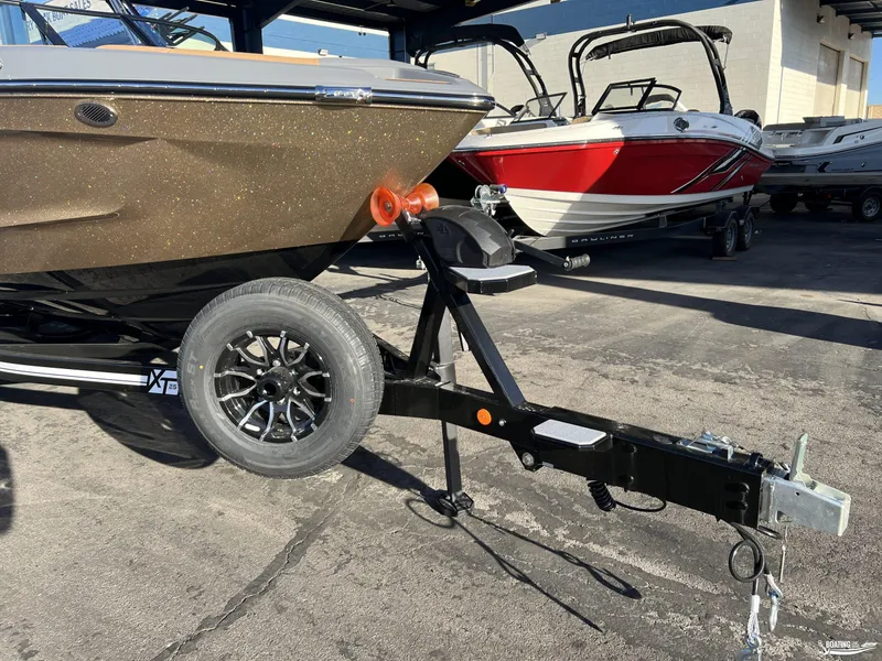 Slide: The Image of 2025 MasterCraft XT25 boat on trailer, parked outdoors, with other boats in the background. - 26