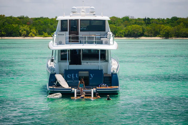 Slide: The Image of 2026 Grand Banks GB 85 yacht anchored in clear turquoise waters, people swimming nearby. - 1