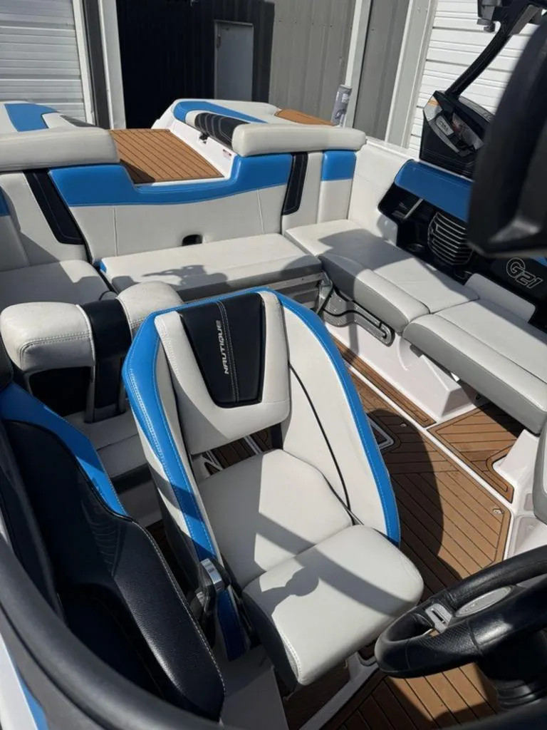 Slide: The Image of 2015 Nautique G21 boat interior with blue and white seating, wood flooring, and steering wheel. - 11