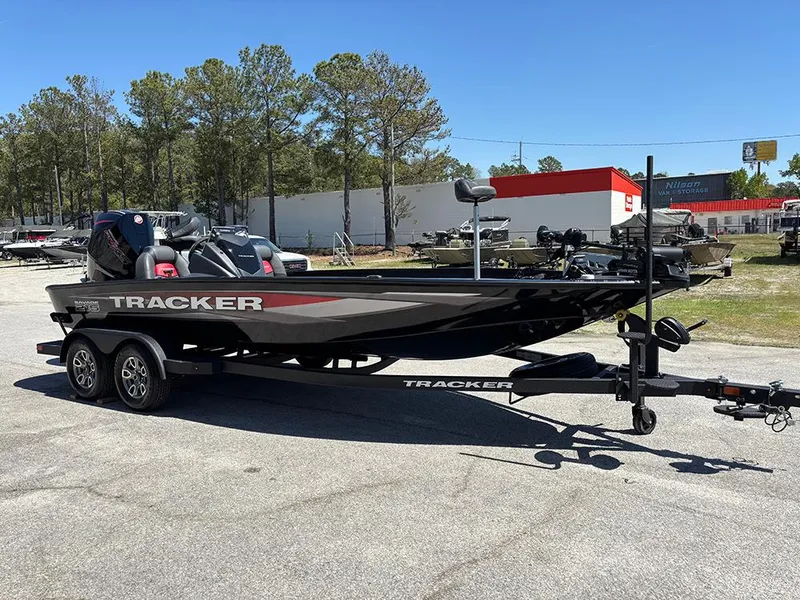 Slide: The Image of 2025 Tracker Savage 215 boat on trailer, parked outdoors, surrounded by trees and buildings. - 5