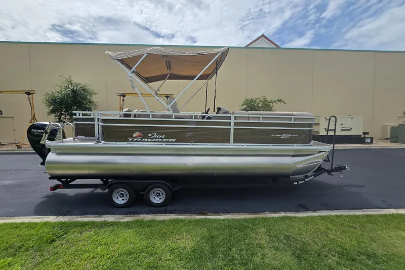 Slide: The Image of 2025 Sun Tracker SportFish 22 XP3 pontoon boat with canopy on trailer, parked outdoors. - 78