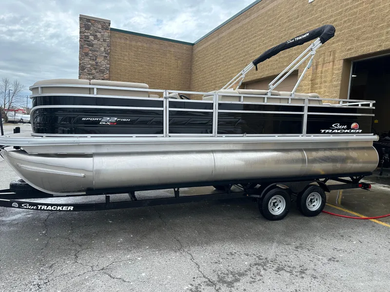 The Image of 2025 Sun Tracker SportFish 22 XP3 pontoon boat on trailer, parked outside a building. - 0