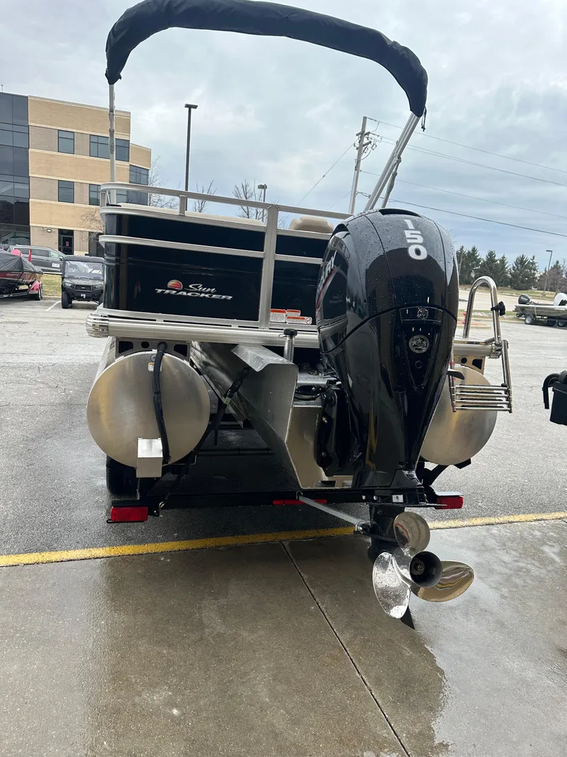 Slide: The Image of 2025 Sun Tracker SportFish 22 XP3 pontoon boat with outboard motor, parked outdoors. - 2