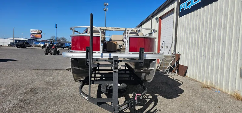 Slide: The Image of 2025 Sun Tracker Bass Buggy 16 XL Select pontoon boat on trailer, parked outside a building. - 2
