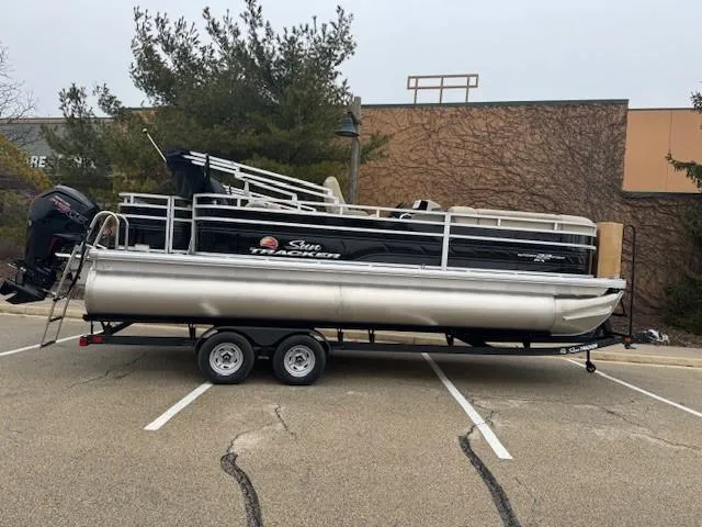 The Image of 2025 Sun Tracker SportFish 22 DLX pontoon boat on a trailer in a parking lot. - 0