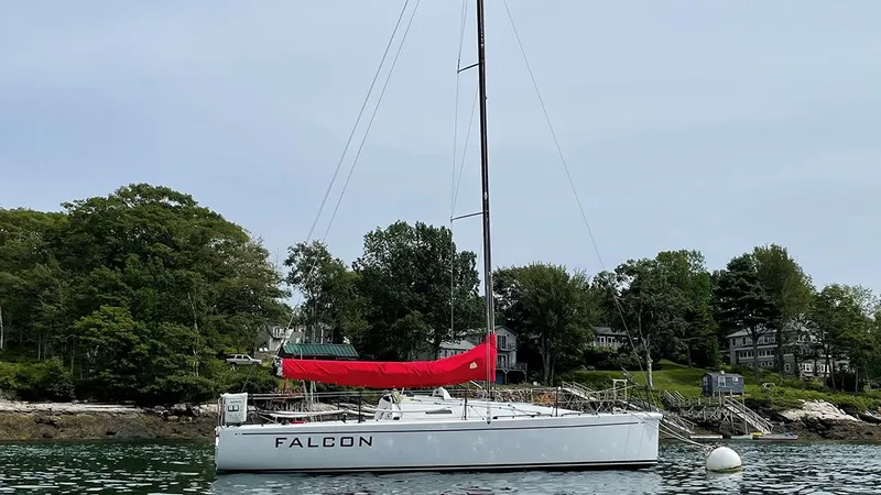 Slide: The Image of Columbia Yacht 32, 2012 model, with red sail cover, moored near a wooded shoreline. - 0