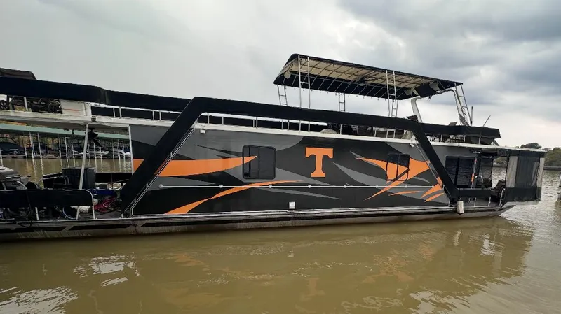 Slide: The Image of 1991 Sumerset 14x60 houseboat with black and orange design on a cloudy day. - 1