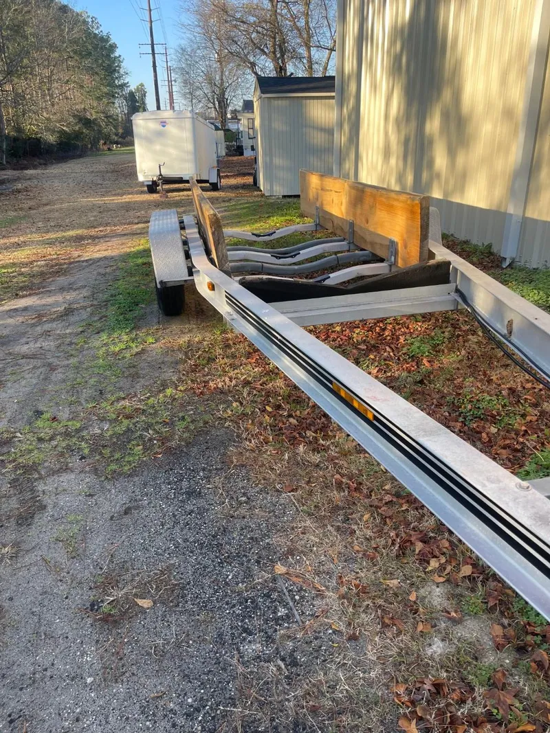 Slide: The Image of Custom Downeast 2011 boat trailer parked on gravel near buildings and trees. - 14