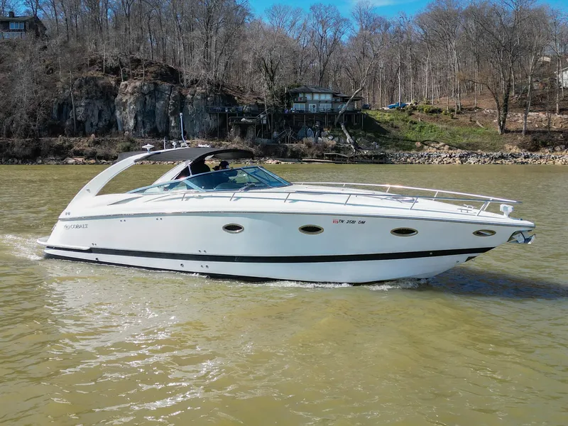 Slide: The Image of 2004 Cobalt 360 boat cruising on a river with wooded shoreline in the background. - 2