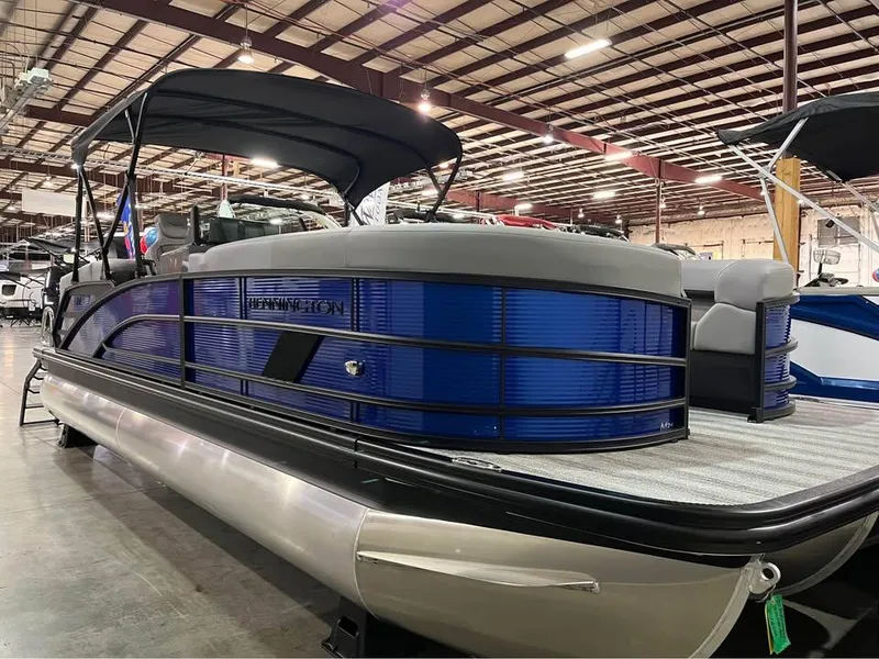 Slide: The Image of 2025 Bennington M 24 Fastback SE pontoon boat in showroom, featuring sleek blue design. - 0