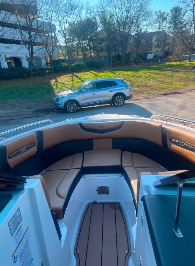 Slide: The Image of 2021 Chaparral 267 SSX boat interior with tan seating, parked SUV in background. - 8