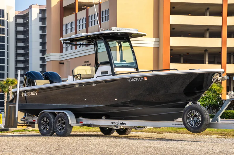 Slide: The Image of 2019 Everglades 273CC boat on trailer, parked near modern buildings. - 3