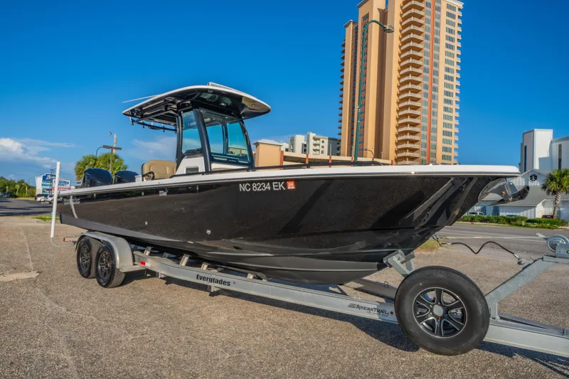Slide: The Image of 2019 Everglades 273CC boat on trailer, parked near tall buildings under clear blue sky. - 7