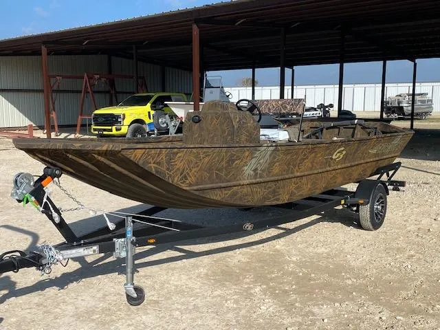Slide: The Image of 2025 G3 Gator Tough 18 CCJ boat on trailer, camo design, parked outdoors. - 2
