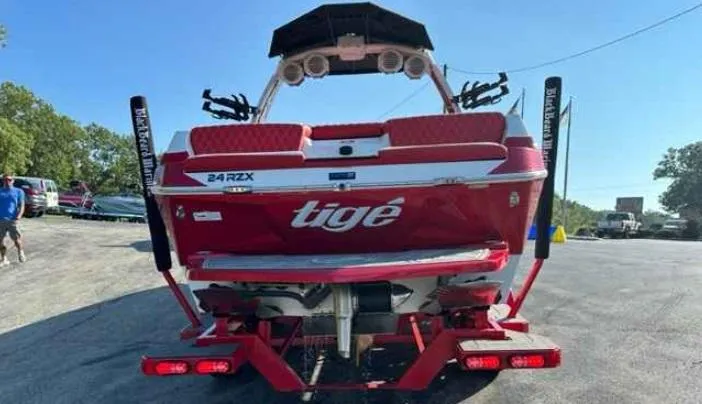 Slide: The Image of 2024 Tigé 24RZX boat, red exterior, rear view with speakers and wakeboard racks. - 2