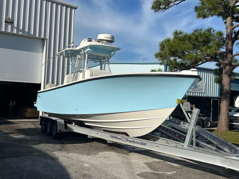 Slide: The Image of 2018 SeaVee 320B boat on trailer, light blue hull, parked outside a warehouse. - 1
