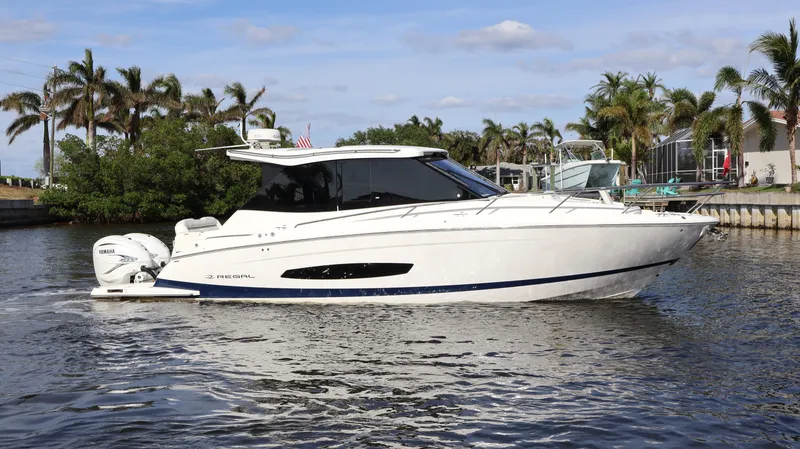 Slide: The Image of 2023 Regal 36 XO boat cruising on a tropical waterway with palm trees. - 5