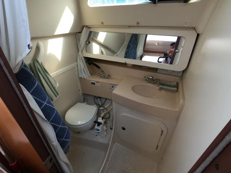 Slide: The Image of 2002 Catalina 310 boat bathroom with sink, toilet, mirror, and shower curtain. - 16