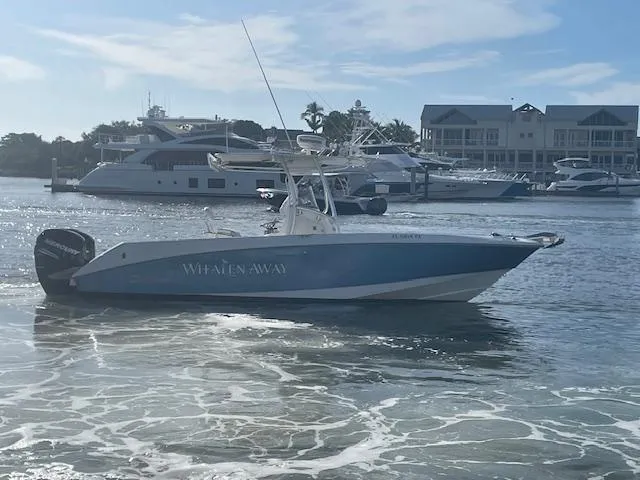 Slide: The Image of 2008 Boston Whaler 270 Outrage boat on water, with marina and yachts in background. - 2