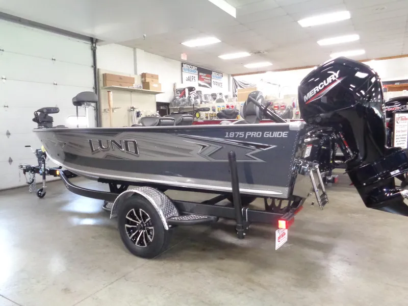 Slide: The Image of 2025 Lund 1875 Pro Guide boat in showroom with Mercury outboard motor. - 1