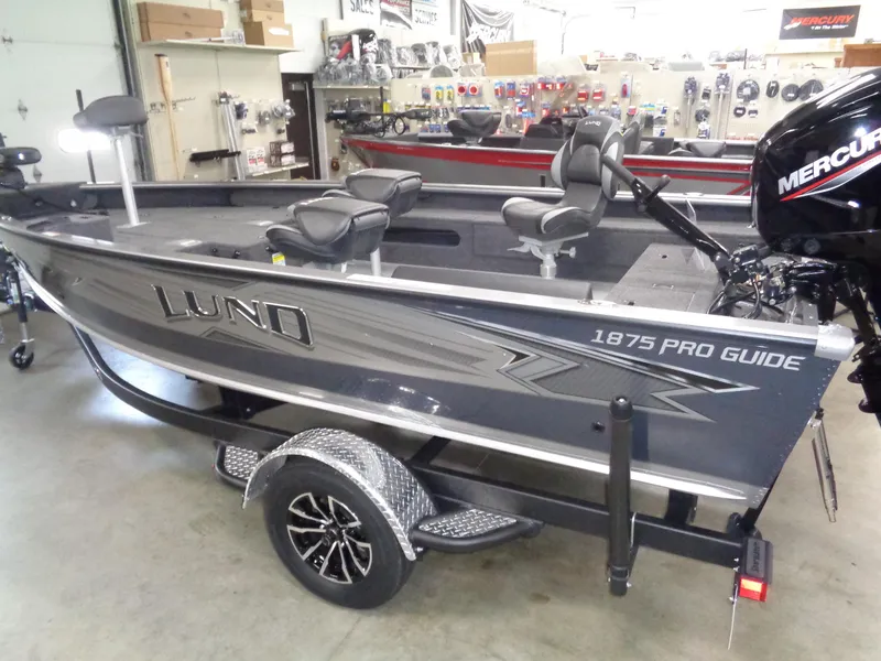 Slide: The Image of 2025 Lund 1875 Pro Guide fishing boat in showroom, featuring Mercury outboard motor. - 34