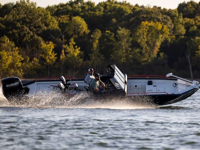 Slide: The Image of 2025 SeaArk ProCat 240 boat cruising on a lake with lush green trees in the background. - 16