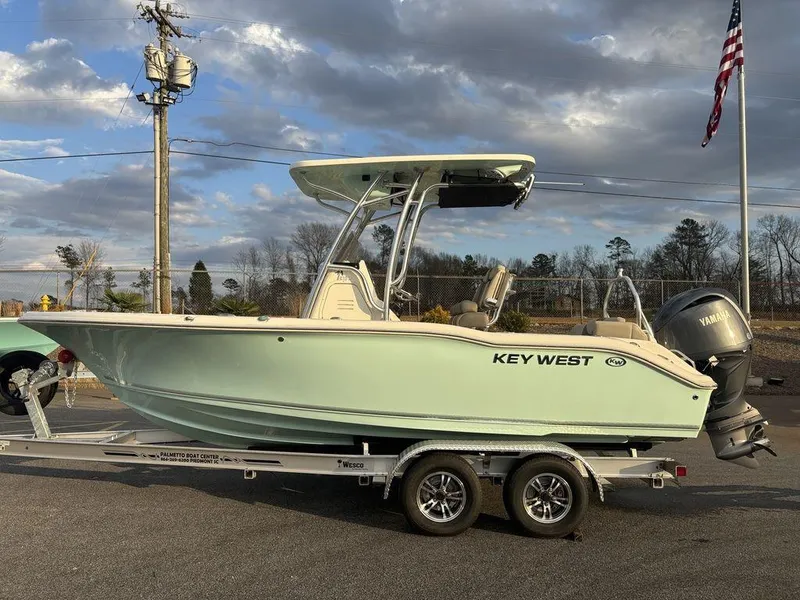 Slide: The Image of 2025 Key West 219fs boat on trailer, parked outdoors under cloudy sky. - 2
