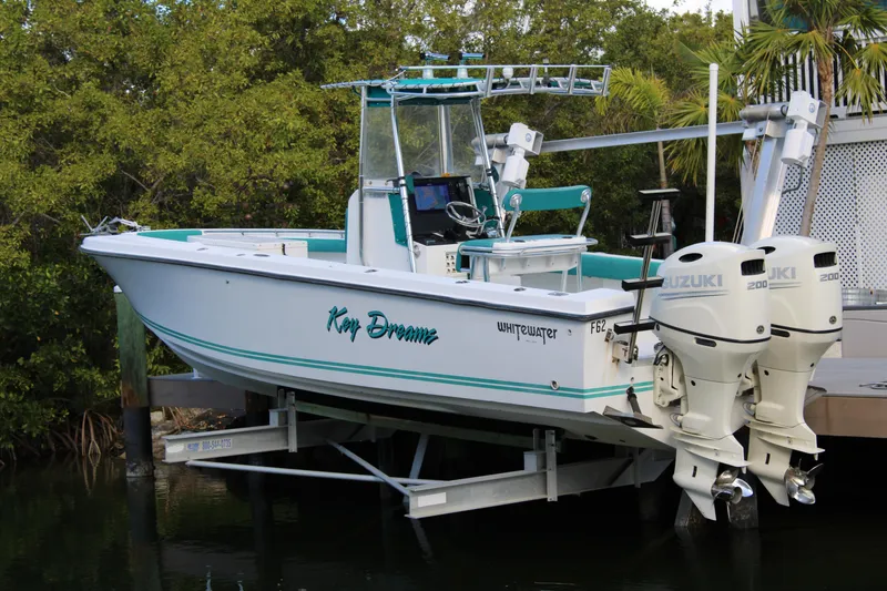 Slide: The Image of 1999 Whitewater 28 Center Console boat with dual Suzuki engines docked by lush greenery. - 2