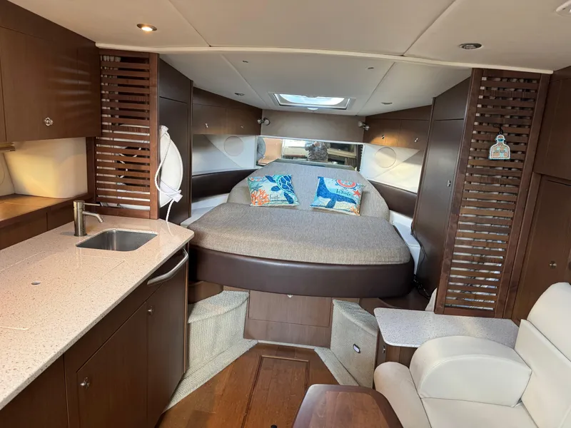 Slide: The Image of 2016 Sea Ray 370 Sundancer cabin interior with bed, kitchenette, and seating area. - 24