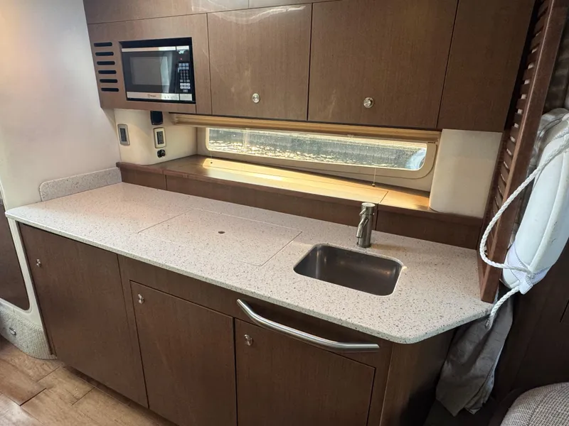 Slide: The Image of 2016 Sea Ray 370 Sundancer galley with modern cabinetry, sink, and microwave. - 25
