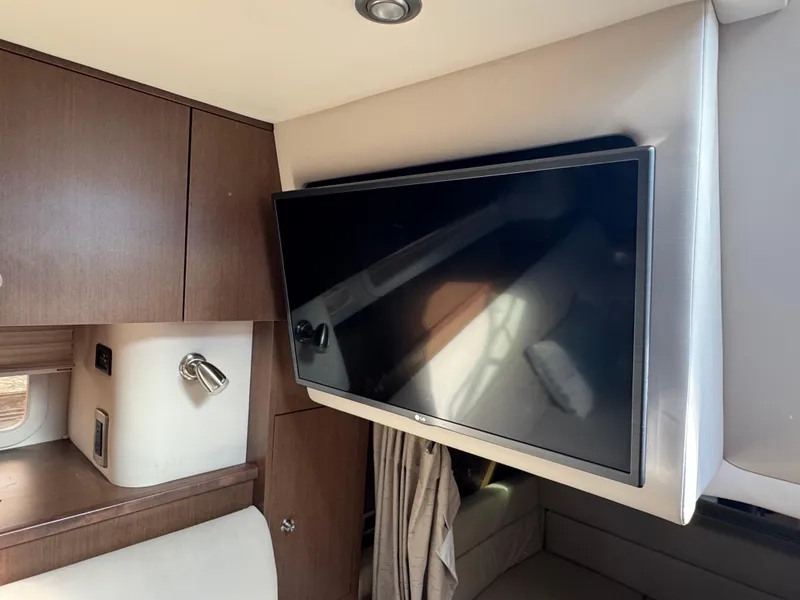 Slide: The Image of Interior of 2016 Sea Ray 370 Sundancer with mounted TV and wooden cabinetry. - 29