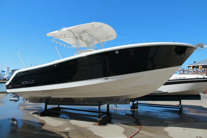 Slide: The Image of 2013 Robalo R300 Center Console boat on display, black hull, white top, sunny day. - 1