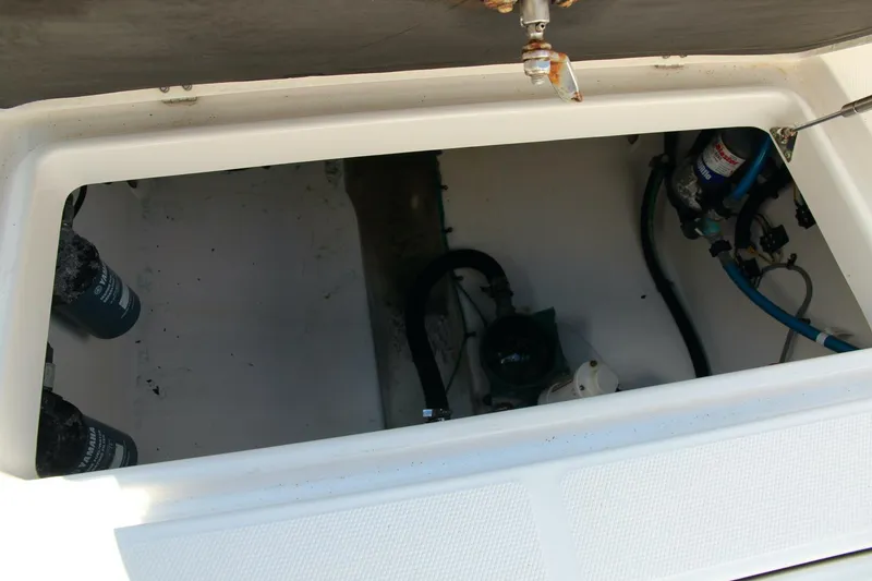 Slide: The Image of 2013 Robalo R300 Center Console boat storage compartment with visible hoses and fittings. - 23