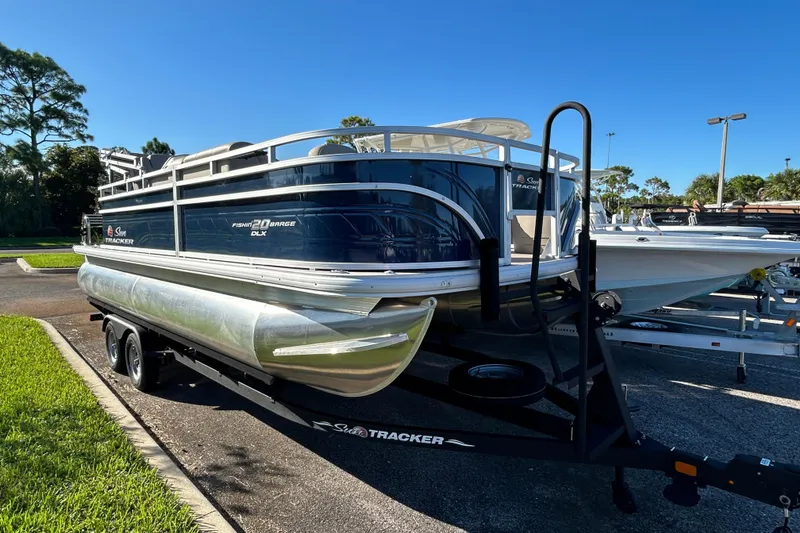 The Image of 2025 Sun Tracker Fishin' Barge 20 DLX pontoon boat on trailer in sunny parking lot. - 0