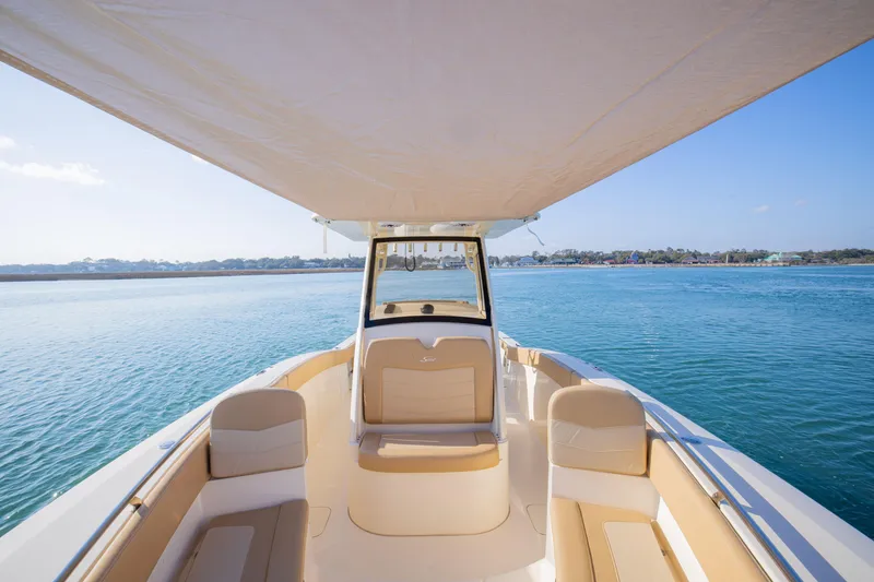 Slide: The Image of 2021 Scout 277 LXF boat interior with seating, under a canopy, on calm water. - 16