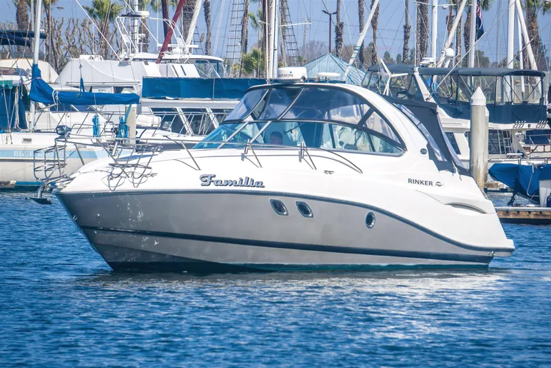 The Image of 2012 Rinker 310 Express Cruiser in marina, surrounded by sailboats and palm trees. - 0