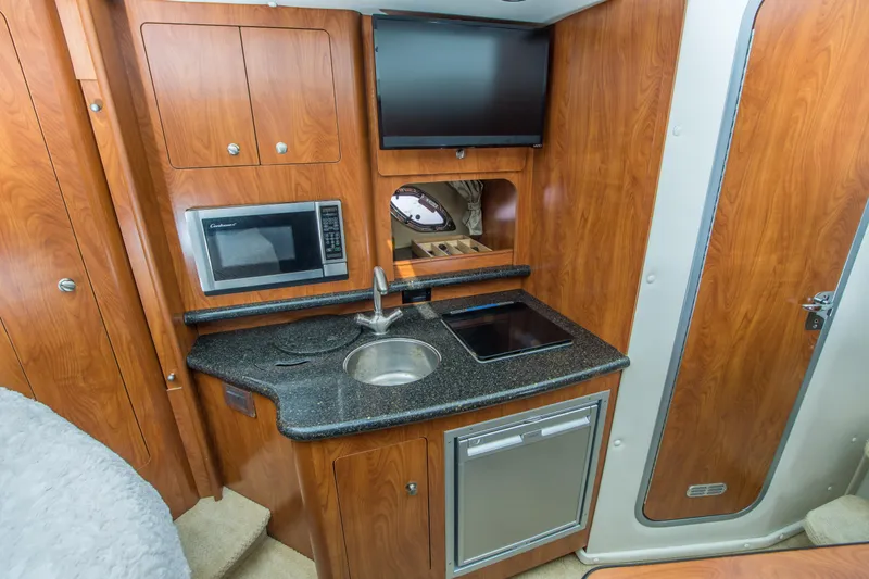 Slide: The Image of 2012 Rinker 310 Express Cruiser interior kitchen with microwave, sink, and wooden cabinetry. - 14