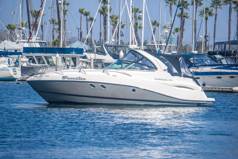 Slide: The Image of 2012 Rinker 310 Express Cruiser in marina, surrounded by sailboats and palm trees. - 2