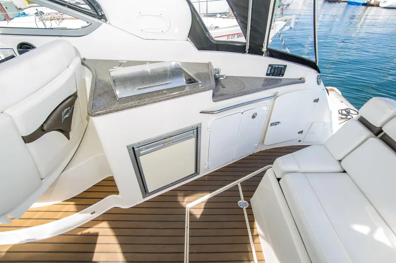 Slide: The Image of 2012 Rinker 310 Express Cruiser interior with kitchenette and seating, featuring sleek design and wood flooring. - 7