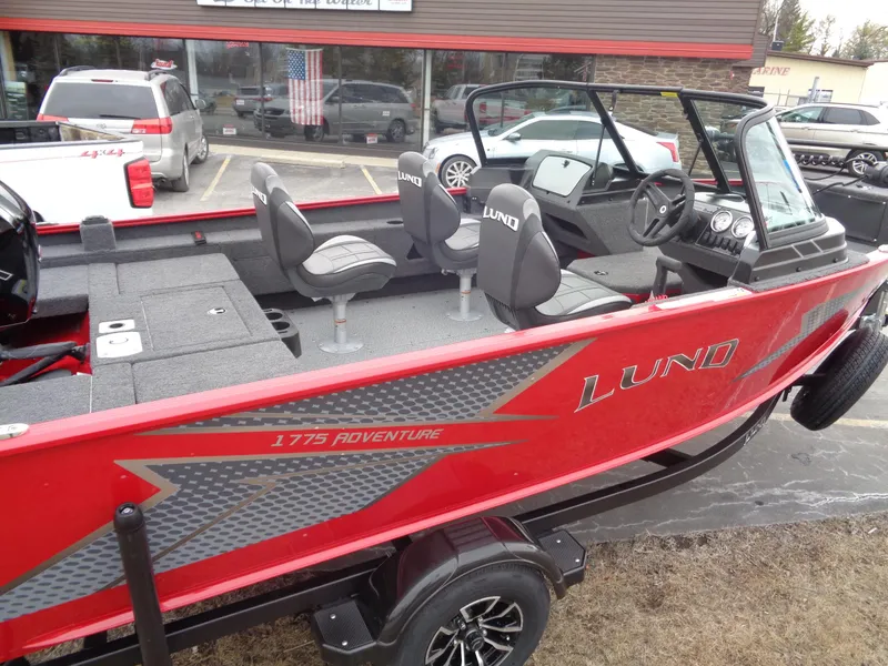 Slide: The Image of 2025 Lund 1775 Adventure Sport boat, red exterior, spacious seating, parked outdoors. - 1
