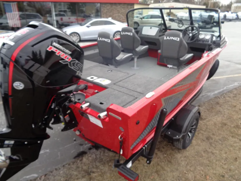 Slide: The Image of 2025 Lund 1775 Adventure Sport boat, red exterior, with motor, parked on grass. - 10